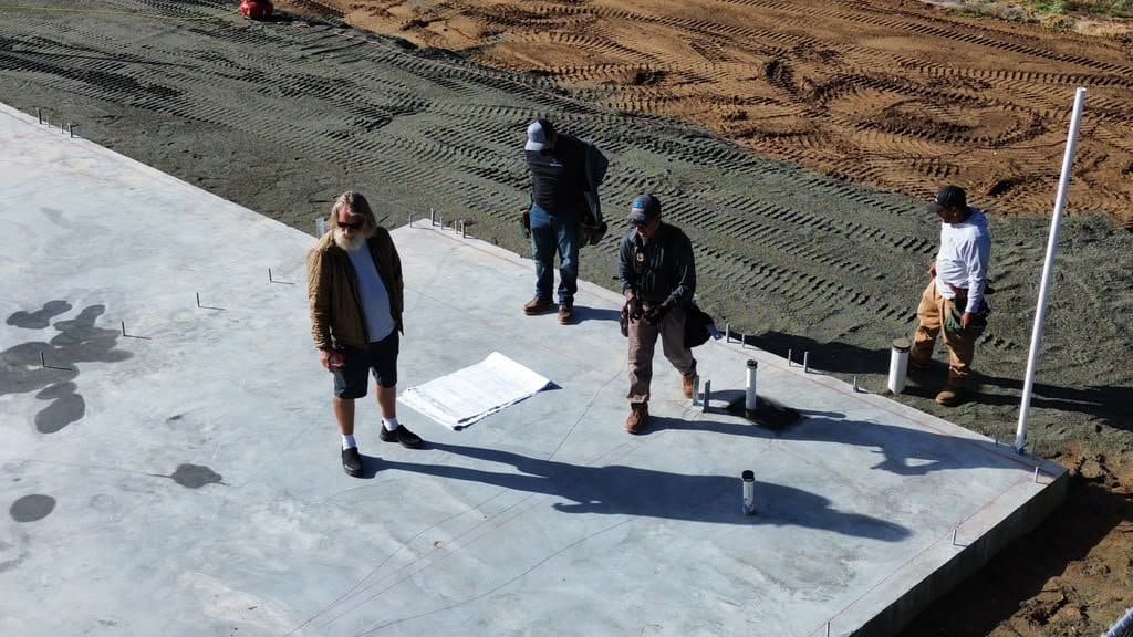 Construction workers on site with concrete foundation and soil background.