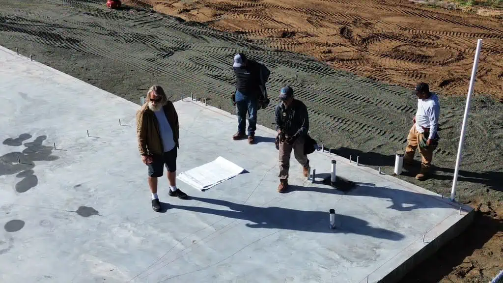 Construction workers on site with concrete foundation and soil background.